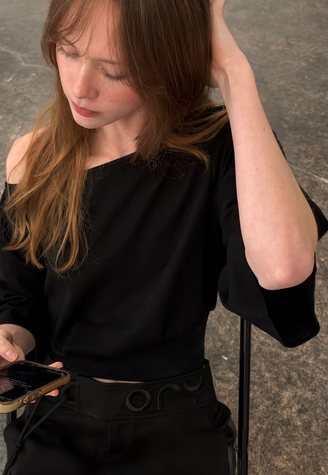 Woman seated wearing the black ORY Kimo Off-Shoulder Top